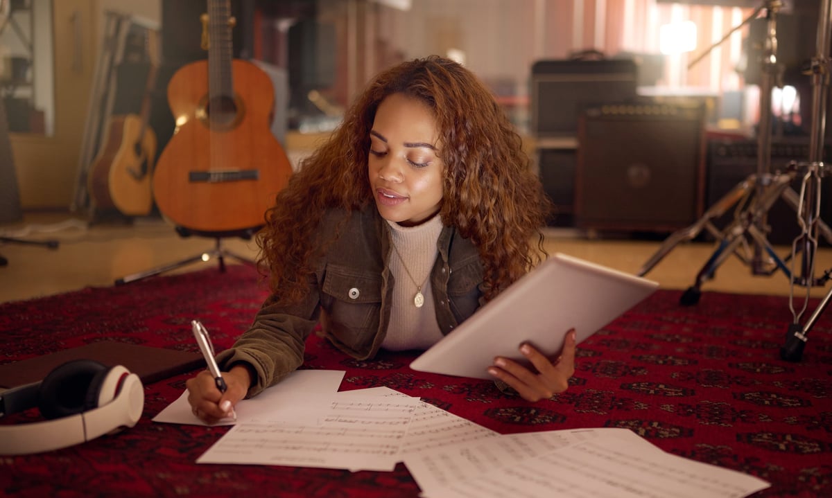 Musician writing lyrics for a song with notebook and digital tablet for composition