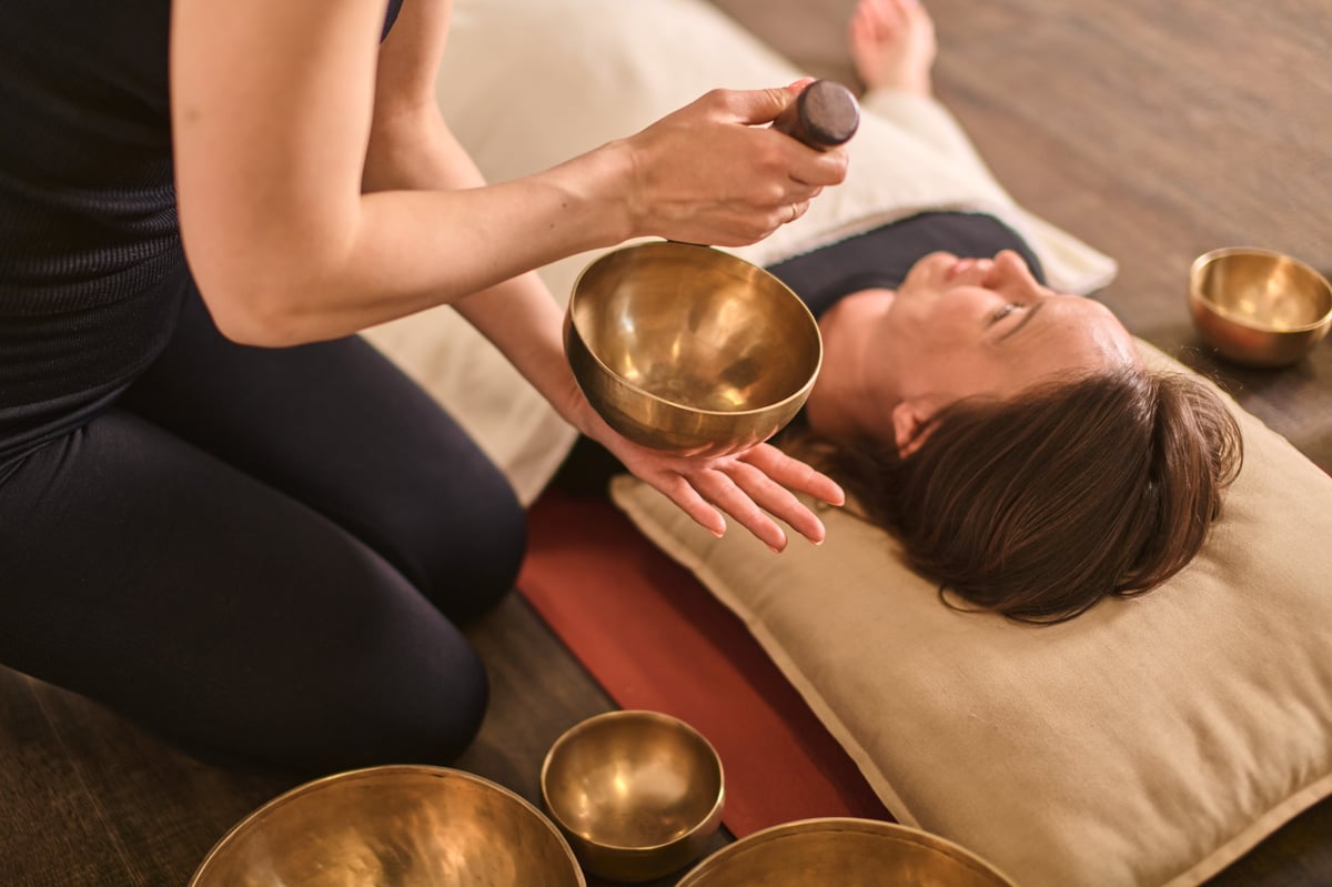Young woman lying on cushion during sound therapy session with singing bowls in warm serene atmosphere