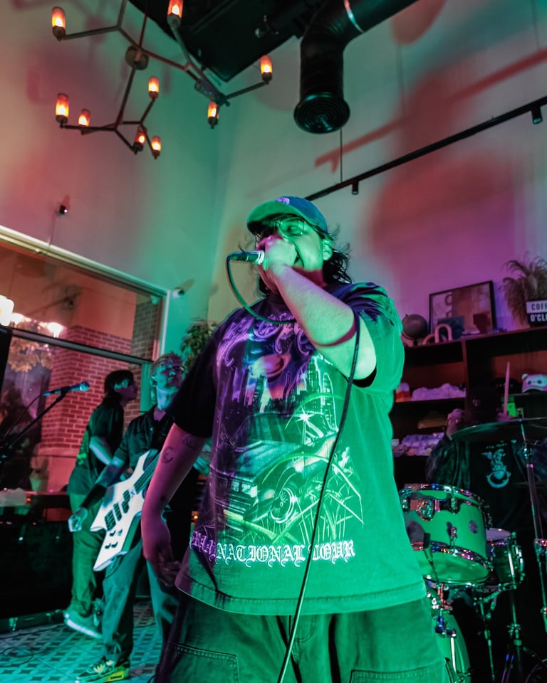 Singer in green cap performing on stage with band under neon pink and green lighting
