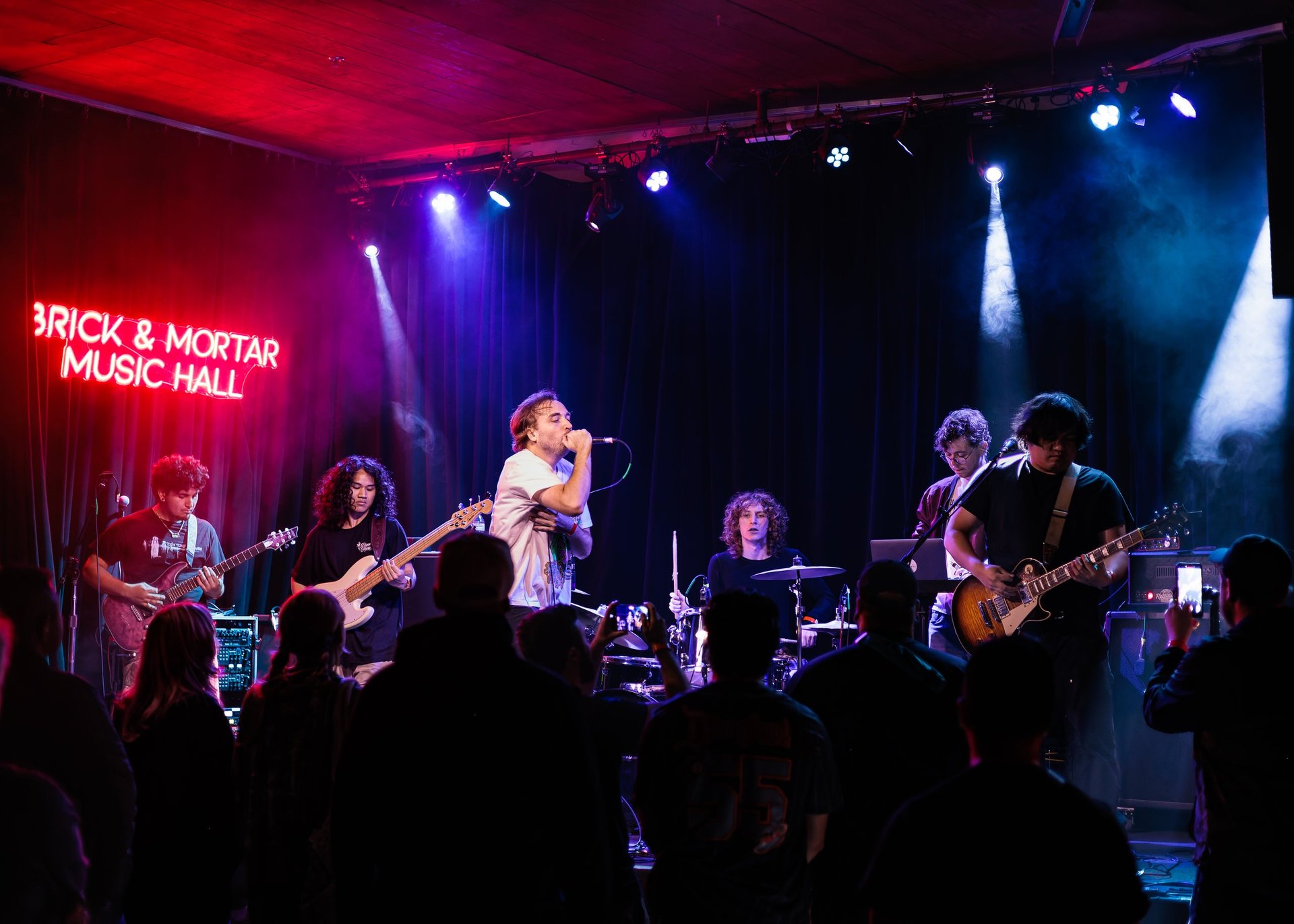 GHSOUND live concert with a full band performing under red and blue stage lights before an audience.