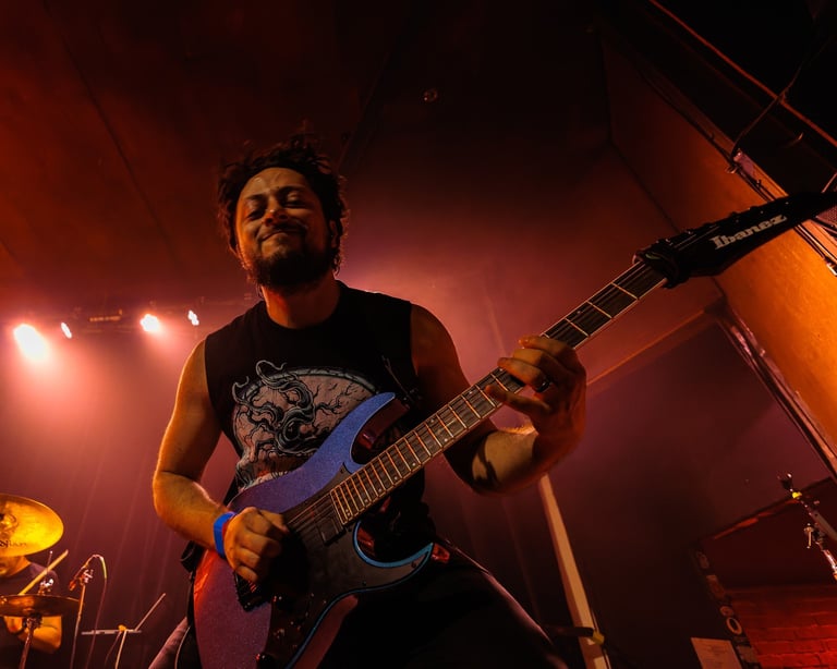 Musician performing on stage with blue electric guitar under warm orange lighting and stage lights