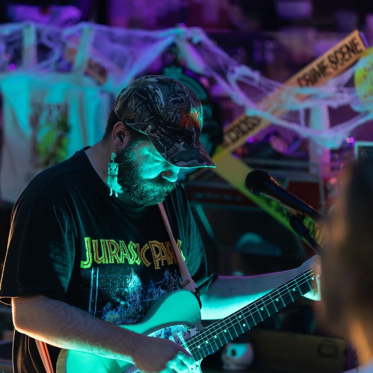 Musician wearing sunglasses playing electric guitar under neon cyan and purple stage lighting with colorful graffiti backdrop