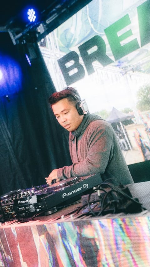 DJ in headphones performing at turntables with blue stage lighting and BRE sign overhead
