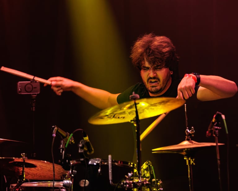 Drummer performing on stage with cymbals raised, illuminated by warm stage lighting