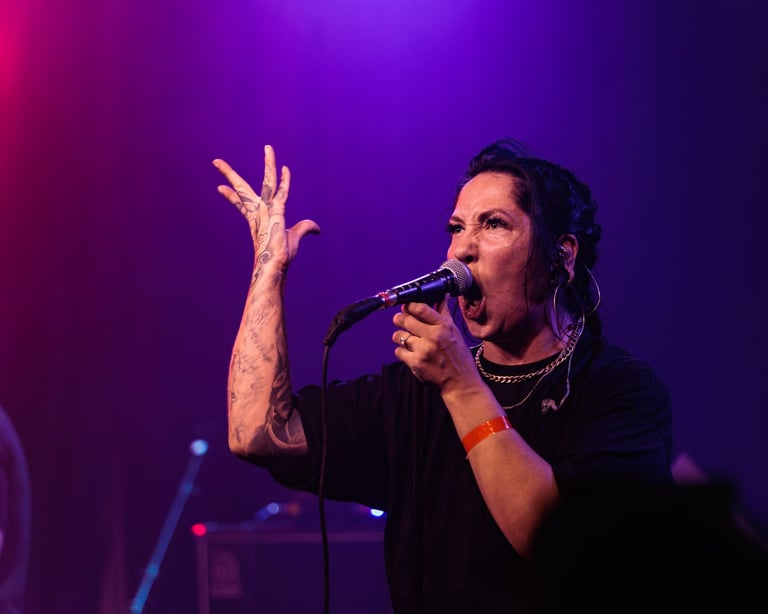Singer performing on stage with microphone, wearing black clothing, gesturing expressively against purple lighting
