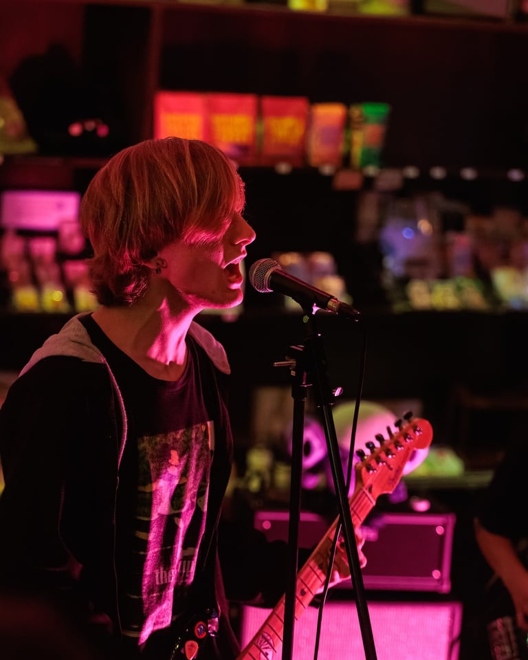 Musician performing on stage with electric guitar under pink and magenta stage lighting in a concert venue