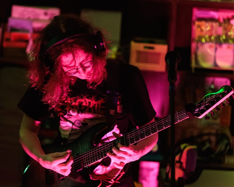 Musician with long hair playing bass guitar under pink neon stage lighting in a dark venue
