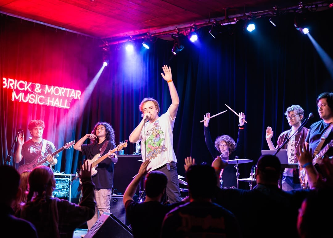 Live band performing on stage at Brick and Mortar Music Hall with colorful red and blue stage lighting and crowd in foreground