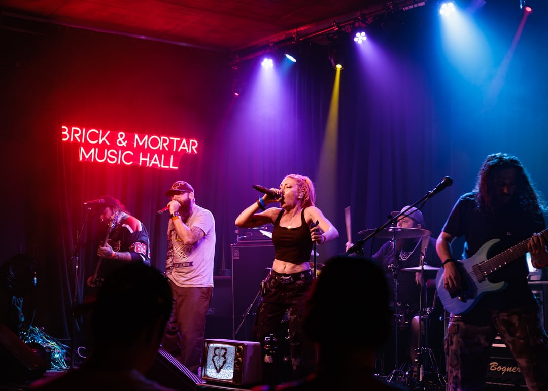 Live band performing on stage at Brick & Mortar Music Hall with colorful stage lighting and audience silhouettes in foreground